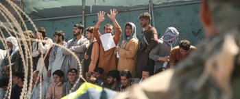 Movie still from “Retrograde” (2022), directed by Matthew Heineman – A group of people standing in a crowd holding up their hands; Medium shot, High angle