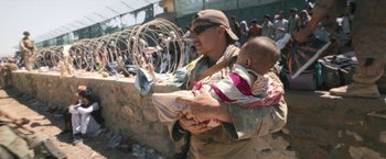 Movie still from “Retrograde” (2022), directed by Matthew Heineman – A man holding a baby in his arms; Medium shot, Low angle