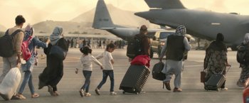 Movie still from “Retrograde” (2022), directed by Matthew Heineman – A group of people walking across a runway with luggage; Wide shot, Low angle