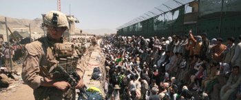 Movie still from “Retrograde” (2022), directed by Matthew Heineman – A crowd of people standing around a fence; Extreme Wide shot, High angle