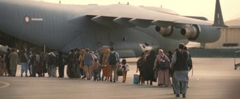 Movie still from “Retrograde” (2022), directed by Matthew Heineman – A group of people walking across a runway; Extreme Wide shot, Low angle