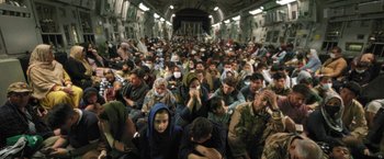 Movie still from “Retrograde” (2022), directed by Matthew Heineman – A large group of people sitting in a plane; Extreme Wide shot, High angle