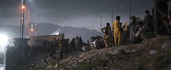 Movie still from “Retrograde” (2022), directed by Matthew Heineman – A group of people standing on top of a hill; Extreme Wide shot, Low angle