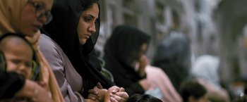 Movie still from “Retrograde” (2022), directed by Matthew Heineman – A woman in a black hijab is holding her hands; Close Up shot, Low angle