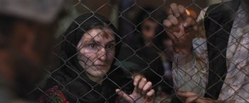 Movie still from “Retrograde” (2022), directed by Matthew Heineman – A woman in a headscarf looking through a fence; Close Up shot, High angle