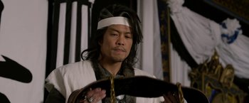 Movie still from “The Man with the Iron Fists” (2012), directed by RZA – A man with long black hair wearing a white headband; Close Up shot, Over the shoulder angle