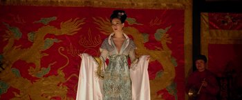 Movie still from “The Man with the Iron Fists” (2012), directed by RZA – A woman in a dress and hat standing in front of a wall; Medium shot, Low angle