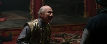 Movie still from “The Man with the Iron Fists” (2012), directed by RZA – An older man wearing a gold and black jacket; Medium shot, Over the shoulder angle
