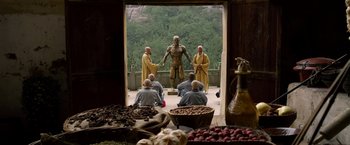 Movie still from “The Man with the Iron Fists” (2012), directed by RZA – A group of men sitting around a statue of a man; Wide shot, Low angle