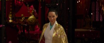 Movie still from “The Man with the Iron Fists” (2012), directed by RZA – A woman in a gold and white outfit standing in front of a wall; Close Up shot, Over the shoulder angle