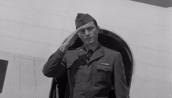 Movie still from “The Manchurian Candidate” (1962), directed by John Frankenheimer – A man saluting while standing in front of an airplane; Medium shot, Low angle