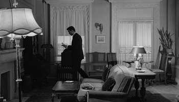 Movie still from “The Manchurian Candidate” (1962), directed by John Frankenheimer – A black and white photo of a man standing in a living room; Wide shot, High angle