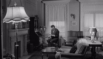 Movie still from “The Manchurian Candidate” (1962), directed by John Frankenheimer – A black and white photo of a man sitting in a living room; Wide shot, High angle