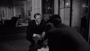 Movie still from “The Manchurian Candidate” (1962), directed by John Frankenheimer – A man in a suit and tie sitting on the floor; Medium shot, Over the shoulder angle