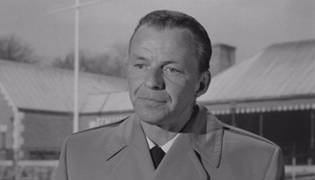Movie still from “The Manchurian Candidate” (1962), directed by John Frankenheimer – An old black and white photo of a man in a trench coat; Close Up shot, Over the shoulder angle