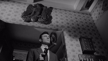 Movie still from “The Manchurian Candidate” (1962), directed by John Frankenheimer – A black and white photo of a man in a suit and tie; Medium shot, Low angle