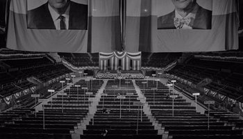 Movie still from “The Manchurian Candidate” (1962), directed by John Frankenheimer – An auditorium with rows of seats in front of a stage with two large banners hanging from the ceiling; Extreme Wide shot, High angle