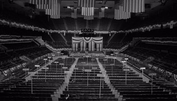 Movie still from “The Manchurian Candidate” (1962), directed by John Frankenheimer – An auditorium with rows and rows of seats in front of an american flag; Extreme Wide shot, High angle
