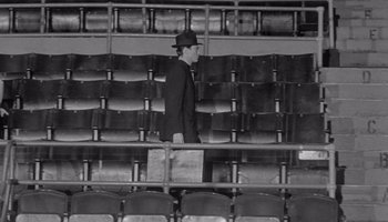 Movie still from “The Manchurian Candidate” (1962), directed by John Frankenheimer – A man in a suit and hat is standing in a stadium; Wide shot, High angle