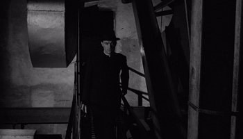 Movie still from “The Manchurian Candidate” (1962), directed by John Frankenheimer – A man wearing a hat standing on some stairs; Wide shot, High angle