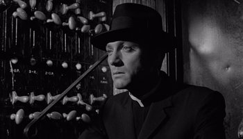 Movie still from “The Manchurian Candidate” (1962), directed by John Frankenheimer – A black and white photo of a man wearing a suit and a hat; Close Up shot, Low angle