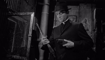 Movie still from “The Manchurian Candidate” (1962), directed by John Frankenheimer – A man in a suit and hat holding a gun and a rifle; Medium shot, Low angle