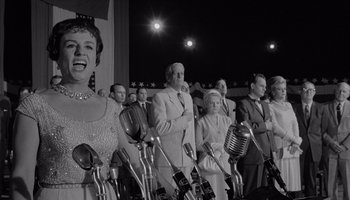 Movie still from “The Manchurian Candidate” (1962), directed by John Frankenheimer – A black and white photo of a group of men and women singing; Medium shot, Low angle