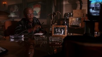 Movie still from “The Mask” (1994), directed by Chuck Russell – A man sitting at a table with a glass of water; Medium shot, Over the shoulder angle