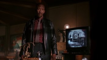 Movie still from “The Mask” (1994), directed by Chuck Russell – A man in a leather jacket and tie standing in front of a tv; Medium shot, Low angle