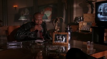 Movie still from “The Mask” (1994), directed by Chuck Russell – A man sitting at a table in front of a picture; Medium shot, High angle