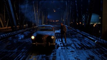 Movie still from “The Mask” (1994), directed by Chuck Russell – A man standing next to an old car on a bridge; Wide shot, High angle