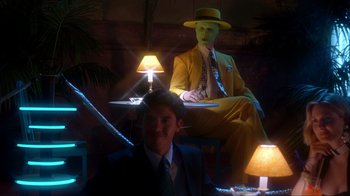 Movie still from “The Mask” (1994), directed by Chuck Russell – A man in a suit sitting in front of a man in a yellow suit sitting in front of a lamp; Medium shot, Low angle