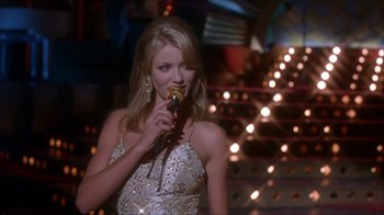 Movie still from “The Mask” (1994), directed by Chuck Russell – A beautiful young lady holding a microphone in her hand; Medium shot, Low angle