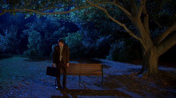 Movie still from “The Mask” (1994), directed by Chuck Russell – A man in a suit and tie holding a briefcase standing next to a park bench; Wide shot, High angle