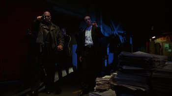 Movie still from “The Mask” (1994), directed by Chuck Russell – A man in a suit and tie standing next to a pile of papers; Medium shot, Low angle