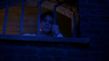Movie still from “The Mask” (1994), directed by Chuck Russell – A man sitting behind bars looking out of a window; Medium shot, Low angle
