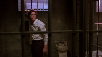 Movie still from “The Mask” (1994), directed by Chuck Russell – A man standing in a jail cell next to a toilet; Medium shot, Low angle