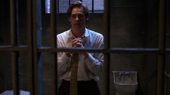 Movie still from “The Mask” (1994), directed by Chuck Russell – A man standing in front of a jail cell with his hands clasped; Medium shot, Low angle
