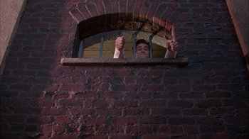 Movie still from “The Mask” (1994), directed by Chuck Russell – A man is looking out of a brick window; Wide shot, Overhead angle