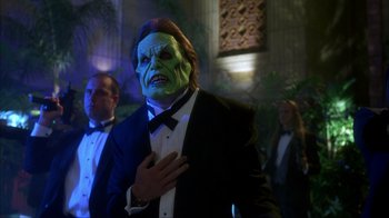 Movie still from “The Mask” (1994), directed by Chuck Russell – A man in a suit and a green mask is holding his hand over his heart; Medium shot, Over the shoulder angle