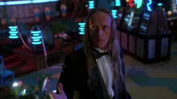 Movie still from “The Mask” (1994), directed by Chuck Russell – A man with long hair wearing a suit and bow tie; Medium shot, Low angle