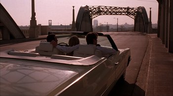 Movie still from “The Mask” (1994), directed by Chuck Russell – A group of people riding in the back of a car; Wide shot, Over the shoulder angle