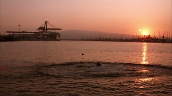 Movie still from “The Mask” (1994), directed by Chuck Russell – A person swimming in a body of water at sunset; Extreme Wide shot, Low angle