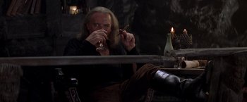 Movie still from “The Mask of Zorro” (1998), directed by Martin Campbell – A man sitting at a table with a cigarette in his mouth; Medium shot, Low angle