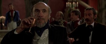 Movie still from “The Mask of Zorro” (1998), directed by Martin Campbell – An old man with a beard and mustache holding a glass of wine; Close Up shot, Over the shoulder angle