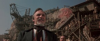 Movie still from “The Mask of Zorro” (1998), directed by Martin Campbell – An older man in a suit and tie standing in front of a wooden structure; Close Up shot, Low angle
