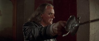 Movie still from “The Mask of Zorro” (1998), directed by Martin Campbell – A man with long grey hair holding a metal object; Close Up shot, Low angle