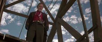 Movie still from “The Mask of Zorro” (1998), directed by Martin Campbell – A man in a suit and a red bandana standing under a wooden structure; Medium shot, Low angle
