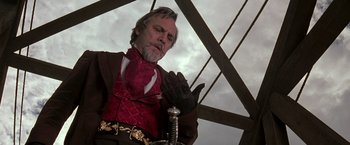 Movie still from “The Mask of Zorro” (1998), directed by Martin Campbell – An older man in a red shirt and a red tie holding a sword; Medium shot, Low angle