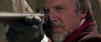 Movie still from “The Mask of Zorro” (1998), directed by Martin Campbell – An older man holding a gun while wearing gloves; Close Up shot, Over the shoulder angle